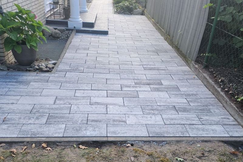 Gepflasterter Weg aus grauen Platten entlang einer Hauswand bis zum Eingang
