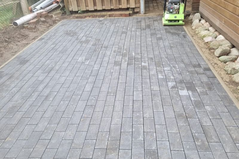Fertig verlegte Pflasterfläche aus grauem Rechteckpflaster vor einem Gartenhaus