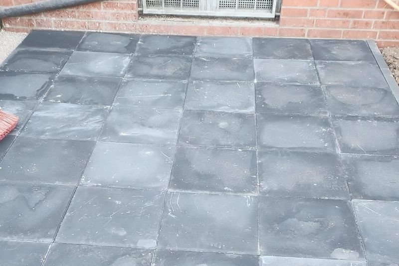 Terrasse aus anthrazitfarbenen Platten direkt an einer Ziegelwand